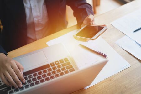 Hand of asian woman business hold smart mobile phone and using laptop in business group,small...
