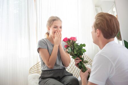 Young caucasian man surprise girlfriend with bunch of rose to celebrate their anniversary wedding...