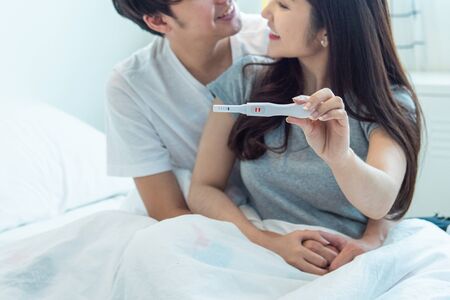 Young happy asian couple with encourage and hug together with pregnancy test.Expecting mom with...
