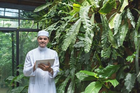 Arab business asian man using tablet, standing in green cafe wear muslim dress freelance business...