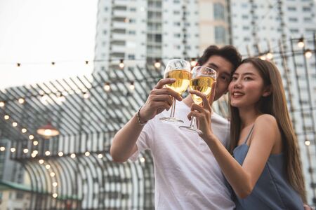 Young asian couple lover have fun dancing and drinking in night party on rooftop floor nightclub hand holding beer bottle and eye contact flirting at couple party.focus on two glasses of wine.の写真素材