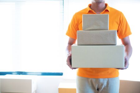 Young delivery asian man in uniform holding and carrying stack of cardboard postel in office.