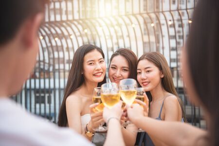 Group of asian multiple gender holding glass of wine chat together with friends while celebrating dance party on outdoor rooftop nightclub,leisure lifestyle of young friendship enjoyment concept.の写真素材