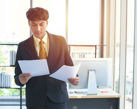 Young asian experienced entrepreneur in formal wear reading financial report and calling to manager...