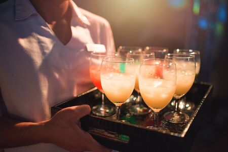 Waitress carry tray of softdrink welcome drink glasses for welcome new customer to hotel of party nightclub and restaurant,sparkling nightlife in background.の写真素材