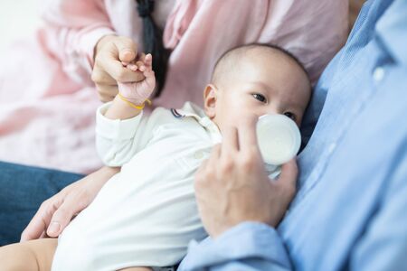 Asian family young father and mother feeding milk baby boy at home. Portrait of asian young couple father mother holding new born infant feeding nursery motherâs day conceptの写真素材