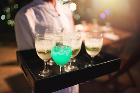 Waitress carry tray of softdrink welcome drink glasses for welcome new customer to hotel of party nughtclub and restaurant,sparkling nightlife in background.の写真素材