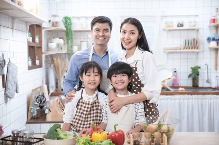 Happy asian father,mother,child standing and smile in kitchen.Healthy parent prepare salad.の写真素材
