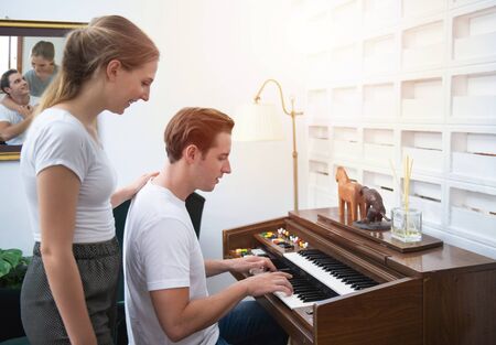 Young caucasian man plays piano in living room listened to by beauty woman with love moment.の写真素材