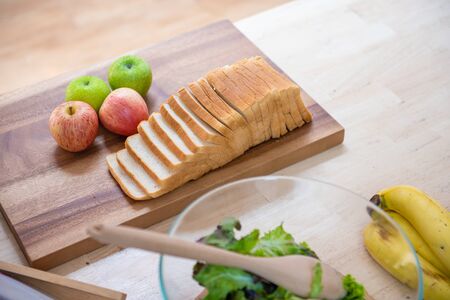 slice white bread on cutting board with apples  and banana with bowl of fresh green salad in kitchen, healthy food concept.の写真素材
