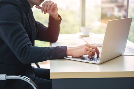 Asian business man hands typing on laptop computer keyboard with business graph diagram data paperwork ,mobile phone and cup of coffee on the desk at modern home office. Digital marketing concept.の写真素材