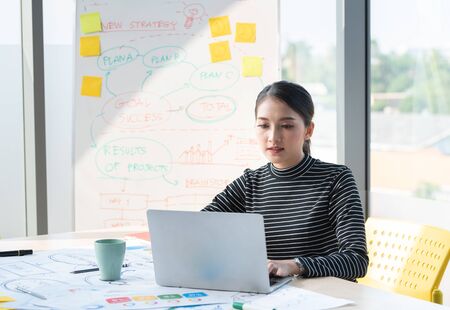 Asian beautiful entrepreneur working and talking video online with laptop and chart board in office...