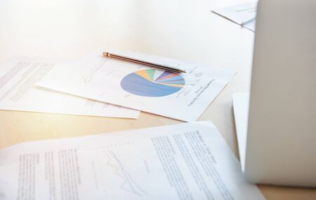 Office desk workplace with pc, paper charts or graph and notebook and pen on wooden table in office.Side view with copy space.の写真素材