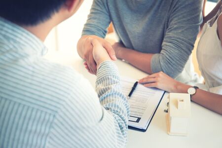 Happy young Asian couple and realtor agent. Cheerful young man signing some documents while sitting at desk together with his wife. Buying new house real estate. Signing good condition contract.の写真素材
