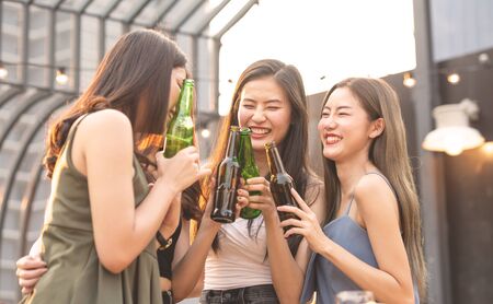 Group of young beautiful happy asian women holding bottle of beer chat together with friends while...