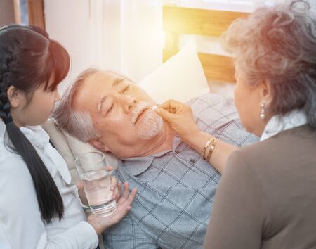 Asian Senior man taking medicines and drinking water while lie on couch at home, health and medicine concept with copy space.の写真素材
