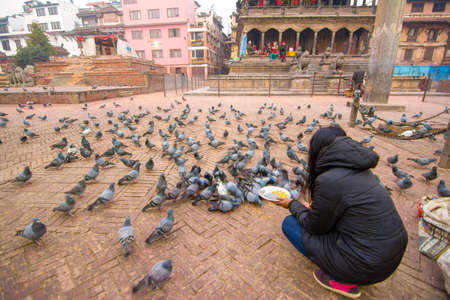 Kathmandu,Nepal - 5 Jan 2016 : Local nepalese people world heritage ancient Patan Durbar Square, Kathmandu, Nepal.One woman sit on knee and feed pigeon on floor.のeditorial素材
