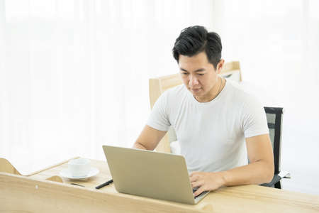 Young asian man working on desk with laptop and mobile phone at sofa at home.