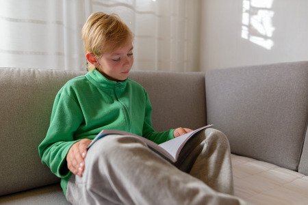 Handsome boy reading book while sitting on sofa at home