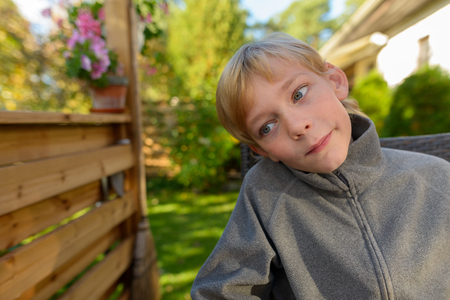 Handsome boy looking down and thinking in the backyard at homeの写真素材