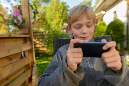 Handsome boy using mobile phone in the backyard at homeの写真素材