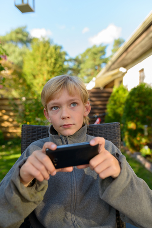 Handsome boy using mobile phone while thinking in the backyard at homeの写真素材