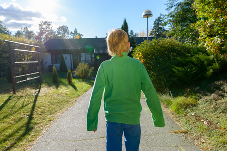 Back view of handsome boy standing in the front yard at homeの写真素材