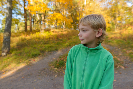 Handsome boy thinking while looking down on path in nature park with autumn treesの写真素材