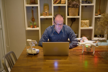 Mature man with drone and laptop in the dining room at home