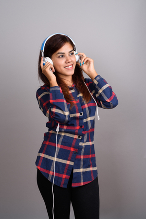 Young beautiful Indian woman listening to music against gray bacの写真素材