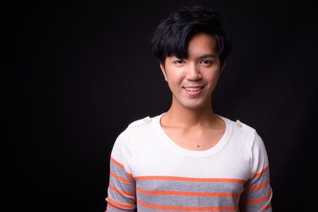 Young handsome Asian man against black backgroundの写真素材