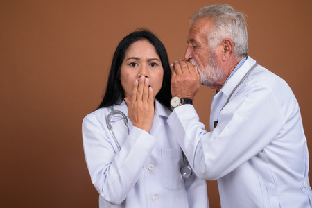 Mature multi-ethnic couple doctors against brown backgroundの写真素材