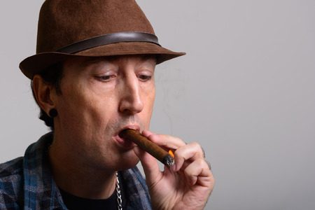 Studio shot of mature gangster man smoking cigar