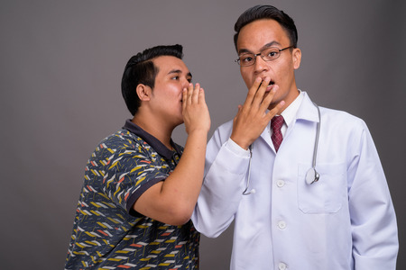 Young multi-ethnic man and young Indian man doctor against grayの写真素材