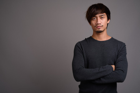 Young Asian man against gray backgroundの写真素材