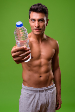 Young handsome Hispanic man shirtless against green backgroundの写真素材