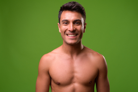 Young handsome Hispanic man shirtless against green backgroundの写真素材