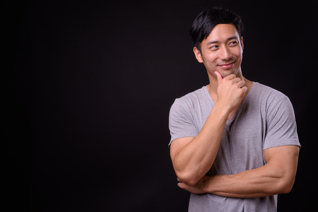Young handsome Asian man against black backgroundの写真素材