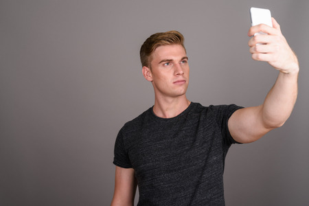 Young handsome man with blond hair wearing gray shirt against grの写真素材