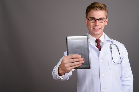 Young handsome man doctor with blond hair against gray backgrounの写真素材