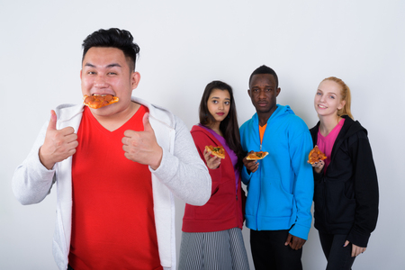 Studio shot of happy young Asian man eating slice of pizza whileの写真素材