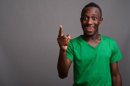 Young African man wearing green shirt against gray backgroundの写真素材