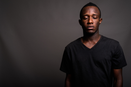 Young African man wearing black shirt against gray backgroundの写真素材