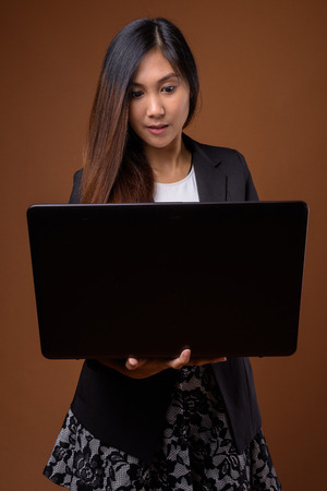 Young beautiful Asian businesswoman against brown backgroundの写真素材