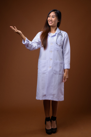 Young beautiful Asian woman doctor against brown backgroundの写真素材