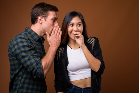 Studio shot of young multi-ethnic couple together against brown