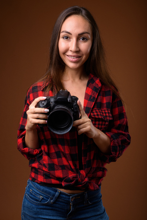 Studio shot of young beautiful woman with camera against brown bの写真素材