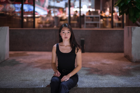 Portrait Of Beautiful Asian Woman Sitting Outdoors At Nightの写真素材