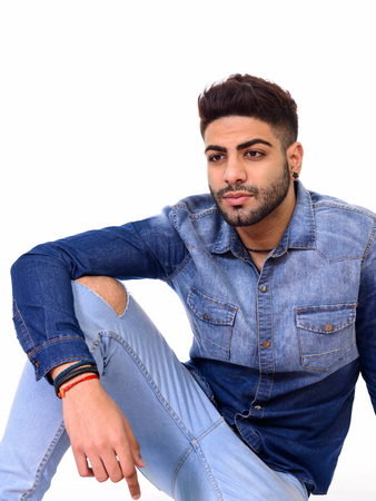 Studio shot of young handsome Indian man sitting on floor isolatの写真素材