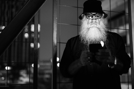 Mature bearded man looking suspicious while using phone in black and whiteの写真素材